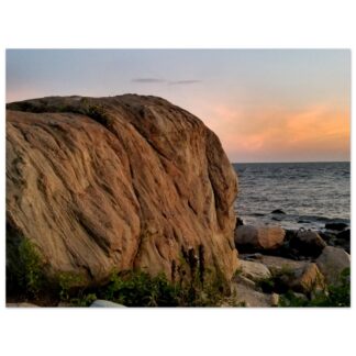A large rock formation overlooking a calm ocean at sunset. The sky is painted in soft orange and pink hues, creating a serene and peaceful atmosphere.