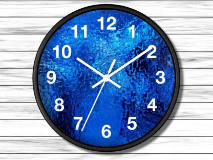 Round wall clock with a textured blue face and white numerals set against a light wooden wall. The clock displays the time as 10:10.