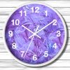 A round wall clock with a white frame features abstract swirls of purple and blue. The clock hands point to 10 and 2, set against a wood panel background.