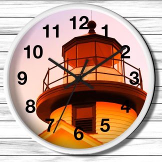 A round nautical wall clock with black numbers and hands features an image of a lighthouse at sunset. The warm orange glow creates a serene, peaceful ambiance.