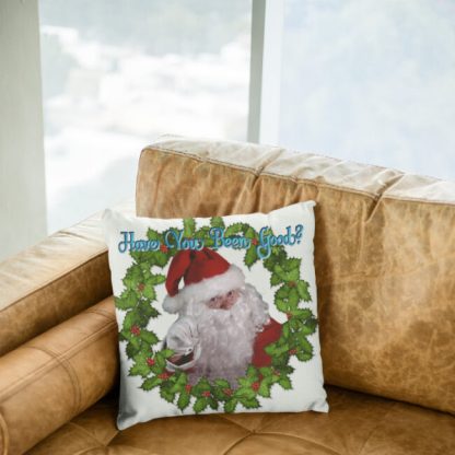 Santa Claus on a Christmas throw pillow points playfully. Surrounded by a festive holly wreath, he asks, "Have You Been Good?" in cheerful blue script.