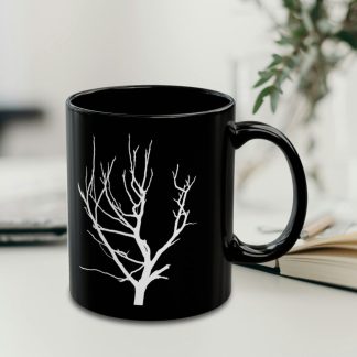 A black coffee mug featuring a white silhouette of a bare tree, set against a softly blurred background with plant.