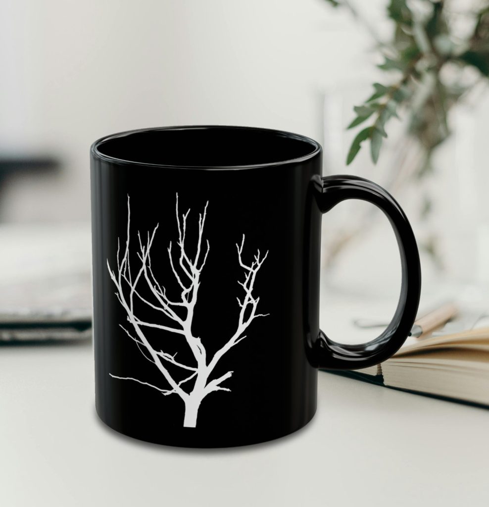 A black coffee mug featuring a white silhouette of a bare tree, set against a softly blurred background with plant.