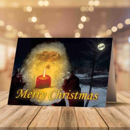 Open Christmas card on a wooden surface with candy canes and pine branches. Card reads, "Merry Christmas" with Santa holding a candle, inside says warm wishes.