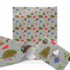 Festive Christmas wrapping paper with Christmas tree and ornament pattern on a gray background. Trees are adorned with colorful decorations. Gift wrapped with twine and heart tag.