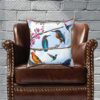 Decorative pillow featuring vibrant birds on branches with pink flowers. Includes kingfishers, a hummingbird, and an oriole under a blue sky. Colorful and lively.