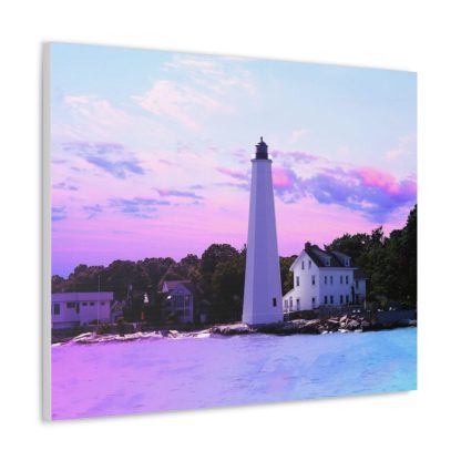 A vibrant canvas print depicts a white lighthouse by the sea, set against a pastel pink and purple sunset. Nearby houses are surrounded by lush greenery. A modern couch with a white cushion sits below, and a green plant peeks from the side, creating a calm and serene atmosphere.