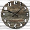 Wall clock with black hands and bold numbers on a round, rustic wood face against a white wood panel background. Time shown is 10:10.