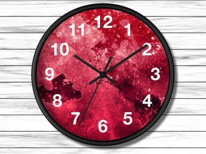 A round clock with a black frame and white numbers. The face has a textured, abstract red pattern. The time is 10:10. Background: white wooden planks.