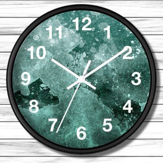 A round wall clock with a black rim features white numerals and hands against a teal green watercolor background. The clock is mounted on a white wooden wall.