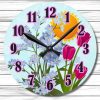 Round clock with pink numbers against a floral background of blue forget-me-nots and pink tulips, set under a bright sun. Warm, cheerful tone.