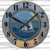 Rustic clock with a porthole design featuring a sailing ship on calm waters. Black numerals and hands contrast against a wooden background.