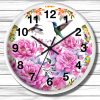Round wall clock with vibrant floral pink peonies and hummingbirds against a white background. Black numerals and hands, set on a wooden plank wall.
