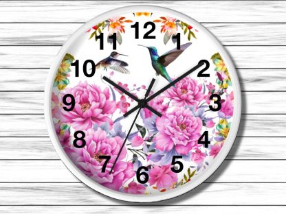 Round wall clock with vibrant floral pink peonies and hummingbirds against a white background. Black numerals and hands, set on a wooden plank wall.