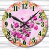 Round wall clock with pink floral design on a light pink background. Black hour and minute hands point to 10:10. Green, black-outlined numbers.