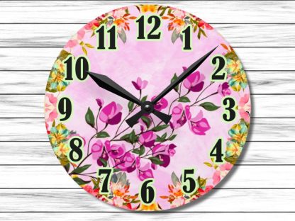 Round wall clock with pink floral design on a light pink background. Black hour and minute hands point to 10:10. Green, black-outlined numbers.