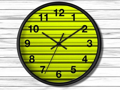 A round wall clock with a black rim features a vibrant yellow background with horizontal lines. It has bold black numbers and hands showing 10:09.