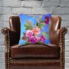 Blue pillow with vibrant floral design featuring pink and purple blossoms and green leaves. The colors convey a cheerful, lively tone.
