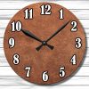 A round wall clock with a textured brown face and bold black and white numbers on a light wood background. The clock shows 10:10.