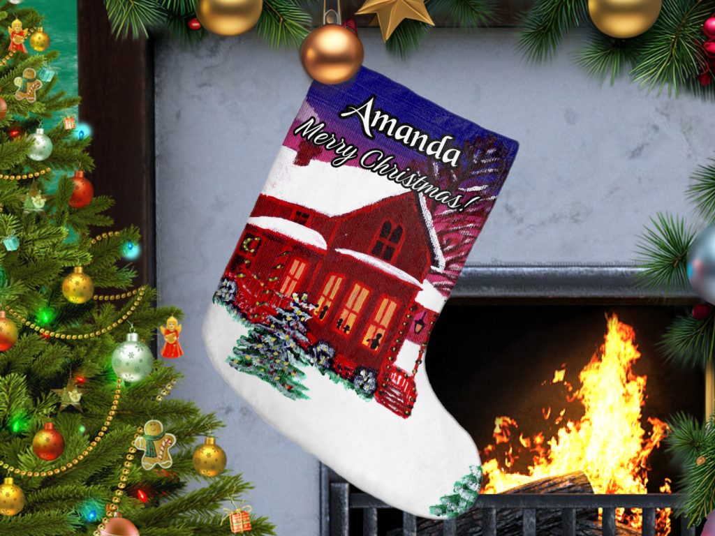 Personalized Christmas stocking with "Merry Christmas" text hangs by a lit fireplace. A painted house in a winter landscape adorns the stocking. A decorated tree with ornaments is on the left, creating a festive, cozy atmosphere.
