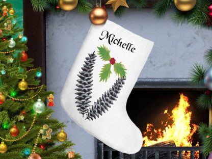 A festive Christmas scene with a white personalized stocking, adorned with pine cones and holly, hanging by a lit fireplace. A decorated Christmas tree glows nearby.