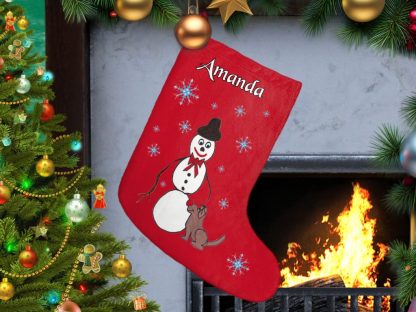 Personalized Red Christmas stocking with a snowman and a dog design hangs by a lit fireplace. Nearby, a decorated tree sparkles with colorful lights and ornaments. Cozy and festive atmosphere.