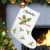 Festive Christmas scene with a personalized stocking by a lit fireplace. Decorated tree with ornaments nearby, creating a cozy holiday atmosphere.