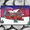 Christmas themed welcome mat features a cozy winter scene with a cottage, snowy roof, and trees against a purple sunset. Text reads “The Smith's WELCOME!” on the cottage. Warm, inviting tone.
