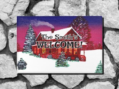 Christmas themed welcome mat features a cozy winter scene with a cottage, snowy roof, and trees against a purple sunset. Text reads “The Smith's WELCOME!” on the cottage. Warm, inviting tone.