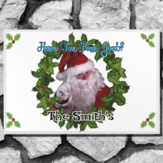 Holiday themed welcome mat with Santa Claus pointing, surrounded by a holly wreath. Text reads "Have You Been Good?" and "The Smith's." Festive and cheerful.