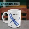 White mug featuring a large blue dragonfly and two smaller ones, with bold, artistic details. The personalized custom name "Sarah" is printed above in black letters, creating a personalized and whimsical design.