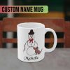 A white mug featuring a whimsical drawing of a snowman with a bow tie and hat, standing by a small brown dog. The personalized custom name "Michelle" is in black script below.