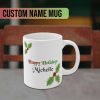 White mug with "Happy Holidays" in festive colors and personalized custom name text "Michelle" in black. Decorated with green holly leaves and red berries, conveying a joyful holiday feel.