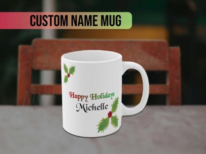 White mug with "Happy Holidays" in festive colors and personalized custom name text "Michelle" in black. Decorated with green holly leaves and red berries, conveying a joyful holiday feel.