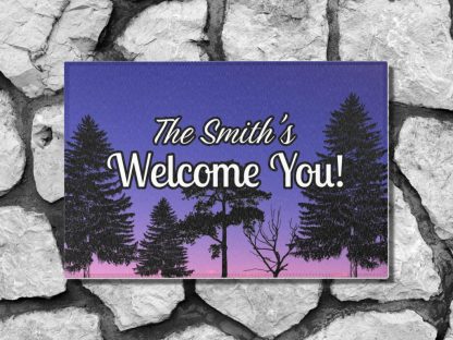 Welcome mat on a stone step with "The Smith's Welcome You!" text over a gradient sky from purple to pink, with silhouettes of tall pine trees, creating an inviting mood.