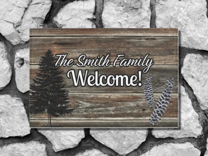 Welcome mat in a rustic wooden panel style on a gray stone step reads "The Smith Family Welcome!" against a stone background. Features a pine tree silhouette and lavender sprigs, conveying warmth.