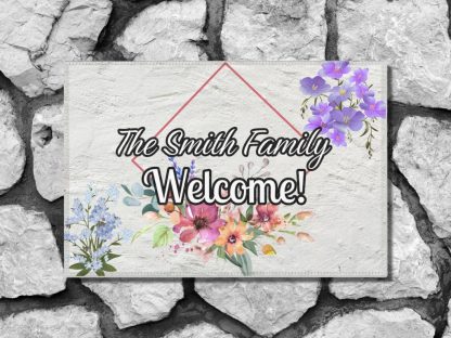 Welcome mat on a stone step with "Welcome" and "The Smith Family" text. Adorned with purple and pink flowers, evoking a warm, inviting tone.