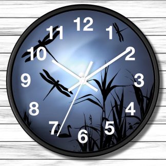 A wall clock with a black frame features silhouettes of dragonflies and reeds against a glowing blue background. White numbers and hands indicate the time.