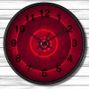 A wall clock with black numbers and hands on a circular red background, featuring concentric glowing circles, on a white wooden panel wall.