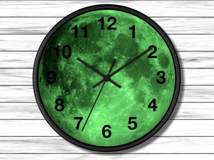 A round wall clock features a glowing green full moon design, black numbers, and hands, set against a white wooden panel background.