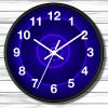A wall clock with a black frame and glowing blue face, white numbers and hands. It hangs on a light wood-paneled wall. The design is modern and striking.