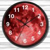 Round wall clock with a vibrant red moon face. Bold black hands point to 10:10. White numerals contrast against the vivid background. Wooden plank wall backdrop.