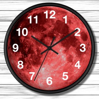 Round wall clock with a vibrant red moon face. Bold black hands point to 10:10. White numerals contrast against the vivid background. Wooden plank wall backdrop.