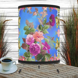Floral-patterned blue lampshade with pink flowers on a wooden table with a cup of coffee. Background features tall grass decor against a white-paneled wall.
