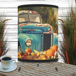 A rustic turquoise vintage truck adorned with pumpkins and gourds in a cozy autumn scene on a lampshade. Nearby, a cup of coffee sits on a wooden surface, with tall grass decor in the background.