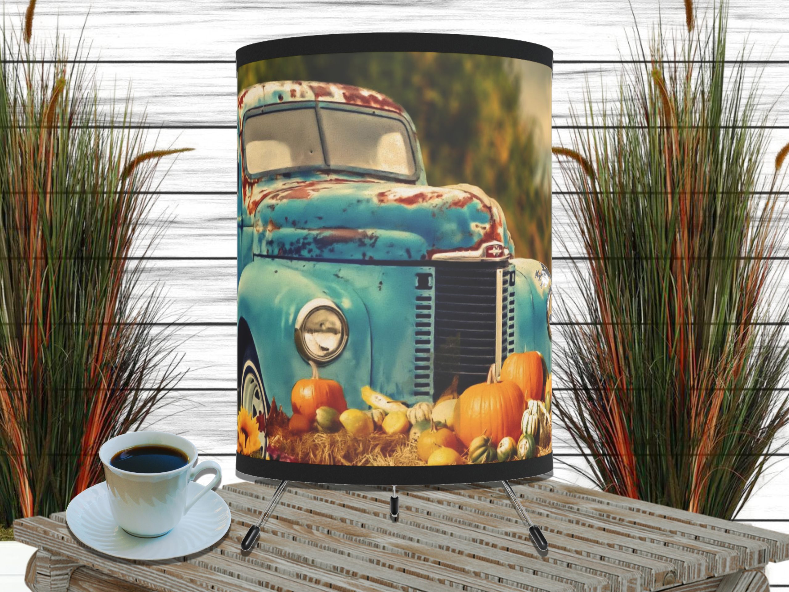 A rustic turquoise vintage truck adorned with pumpkins and gourds in a cozy autumn scene on a lampshade. Nearby, a cup of coffee sits on a wooden surface, with tall grass decor in the background.