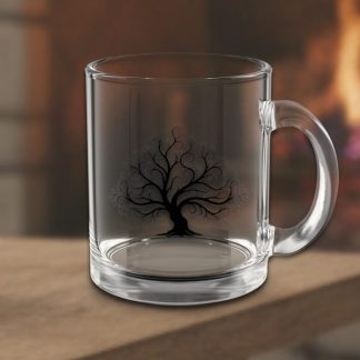 Clear glass mug with intricate black tree design, placed on a wooden surface. A warm, blurred fireplace in the background suggests a cozy atmosphere.