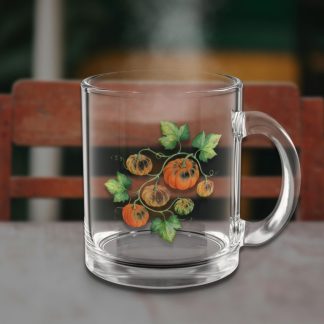 Clear glass mug with painted pumpkins and leaves on a table, faint steam rising, against a warm, blurred chair and background, creating a cozy feel.