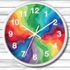 Round wall clock with a white frame, featuring vibrant watercolor swirls in rainbow colors. White numerals and clock hands stand out against the colorful background, creating a dynamic and cheerful visual. The clock is set against a white wooden surface.