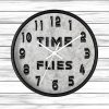 Round wall clock against a white wooden background. The clock face reads "TIME FLIES" between 10 and 2 o'clock, with bold black numbers.